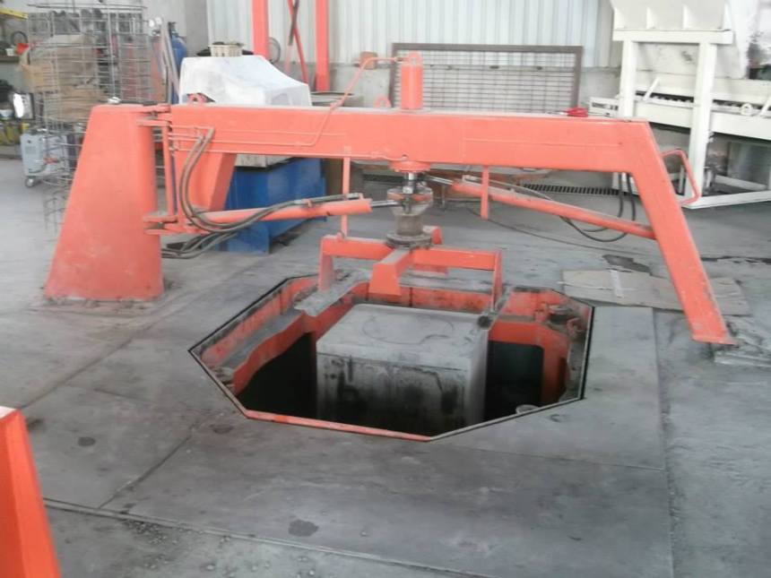 "Fabrika içerisinde yer alan, geniş kollu turuncu renkli bir hidrolik baca menhol makinesi. Makine, yerdeki bir boşluğun içerisinde bulunan gri renkli beton bloğu işlemekte veya yerinden kaldırmaktadır. Görselin altında beyaz harflerle 'Baca Menhol Makinesi' yazmaktadır."